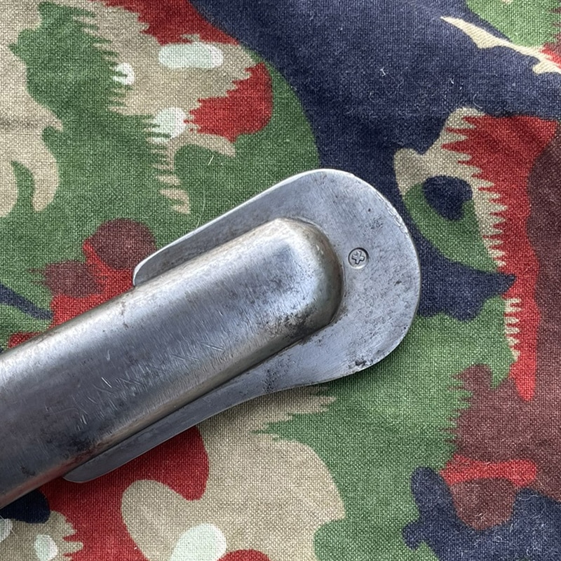 Säbel Ord. 1896 für Mannschaften Waffenfabrik Neuhausen | Fabulafero - Antiquitäten und Einzigartiges Close-up of a metal latch/handle with an oval base and small screw, resting on a colorful patterned fabric.