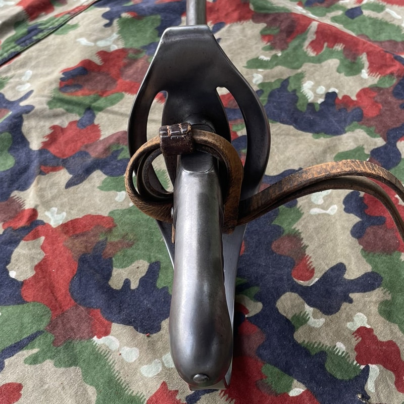 Säbel Ord. 1896 für Mannschaften Waffenfabrik Neuhausen | Fabulafero - Antiquitäten und Einzigartiges Close-up of a vintage bicycle fork crown with a rusted leather strap looped around the steerer, on a camo-patterned background.